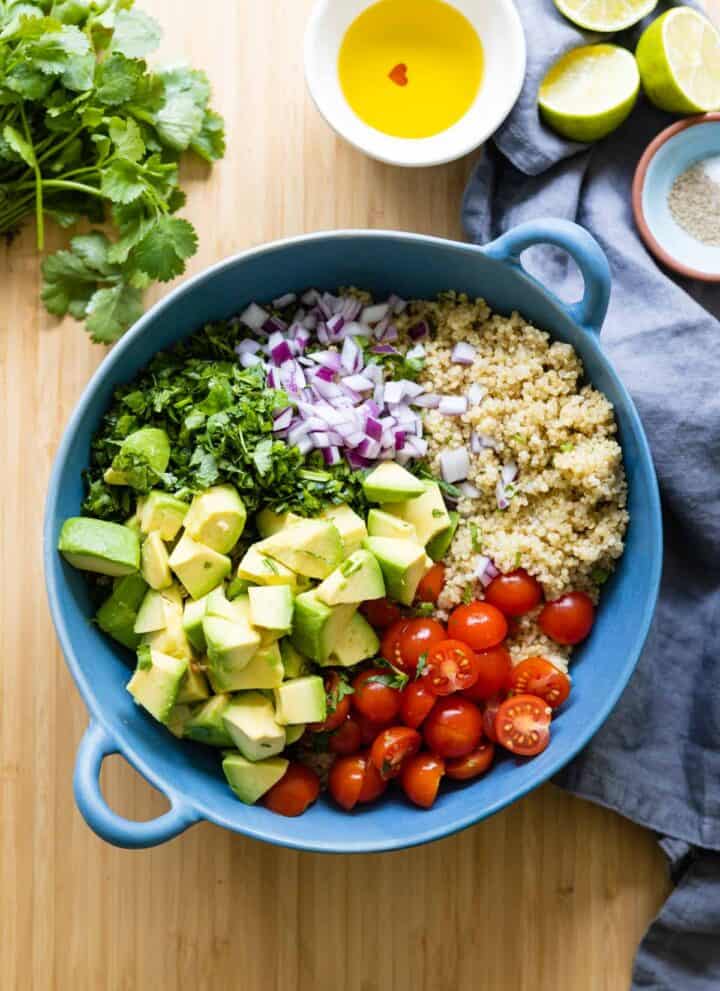 quinoa, avocado, cherry tomatoes, cilantro and red onion in a blue salad bowl.