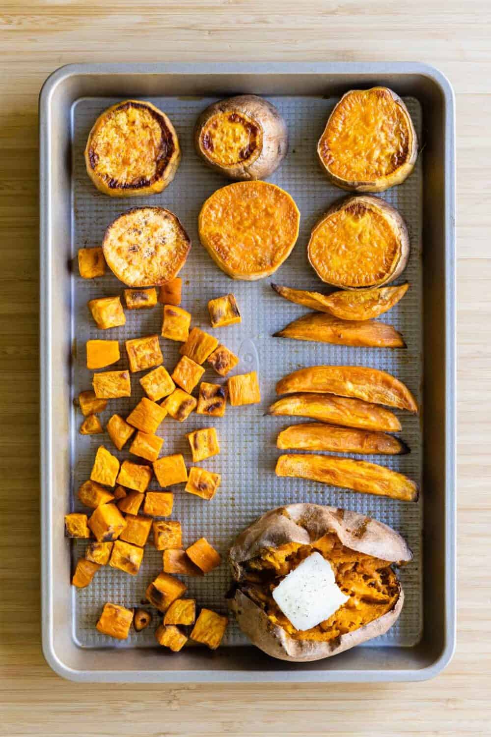 Baked sweet potatoes cut up into rounds, cubes, dice, and as a whole on a baking sheet.