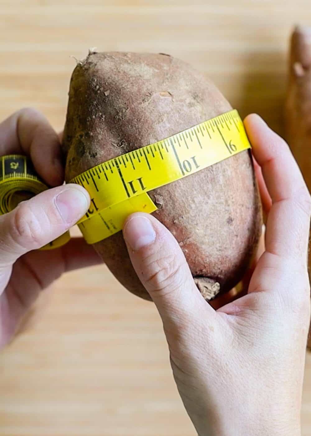 Measuring circumference of sweet potato with a yellow measuring tape.