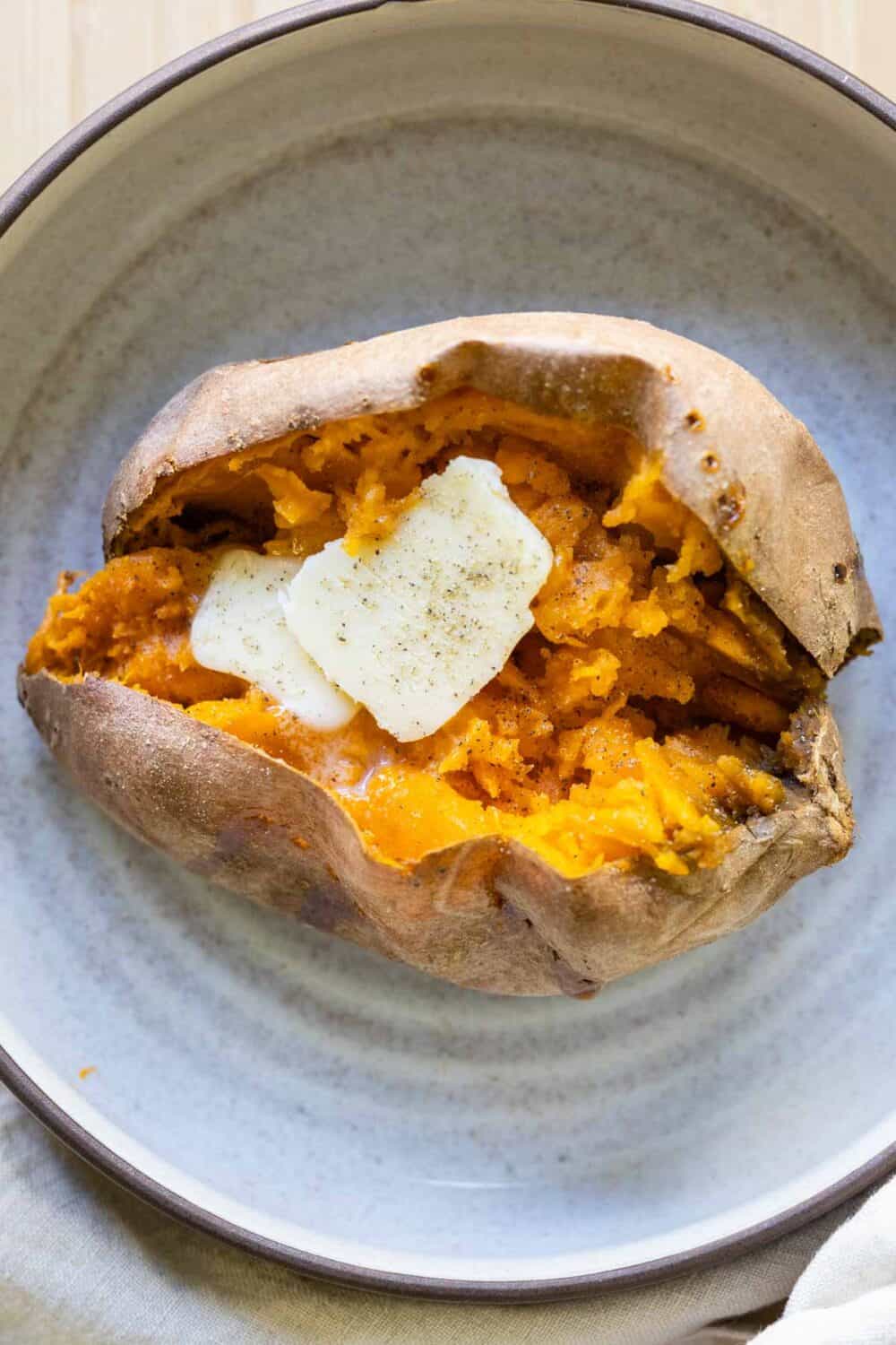 Whole baked sweet potato cut open and a little butter laying on top.