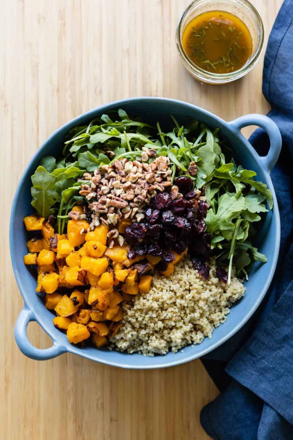 Roasted butternut squash, quinoa, chopped pecans, dried cranberries, arugula in a blue salad bowl.