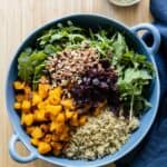 Roasted butternut squash, quinoa, chopped pecans, dried cranberries, arugula in a blue salad bowl.