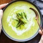 asparagus soup in a grey bowl and spoon taking a bite.