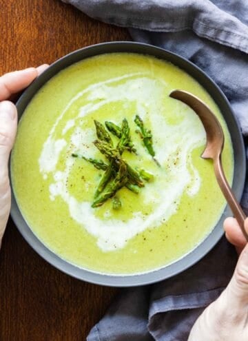 asparagus soup in a grey bowl and spoon taking a bite.