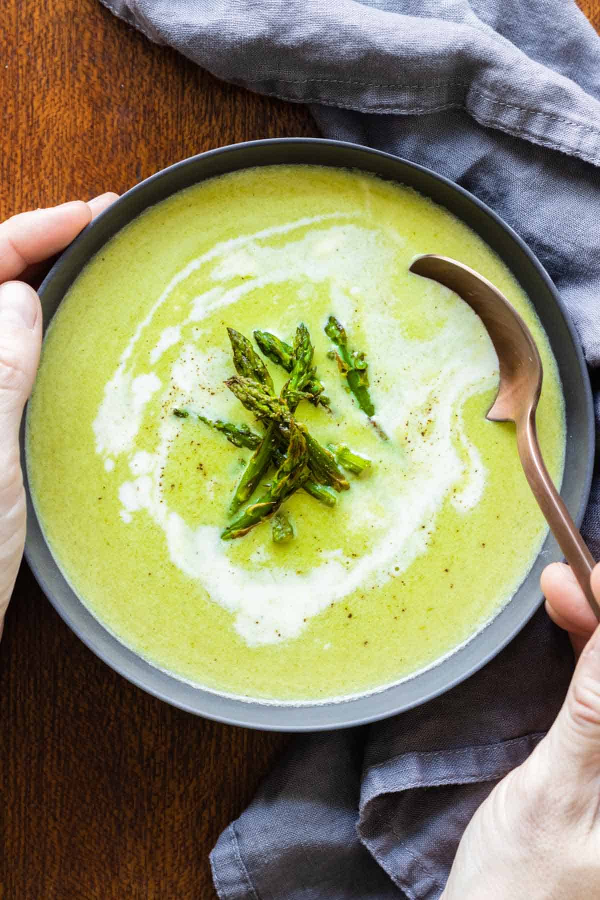 asparagus soup in a grey bowl and spoon taking a bite.