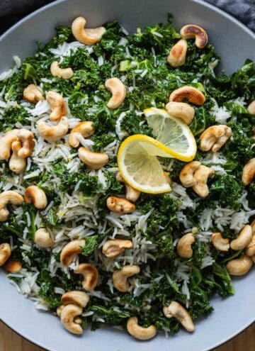 White rice, kale, and cashews in a bowl topped with a slice of lemon.