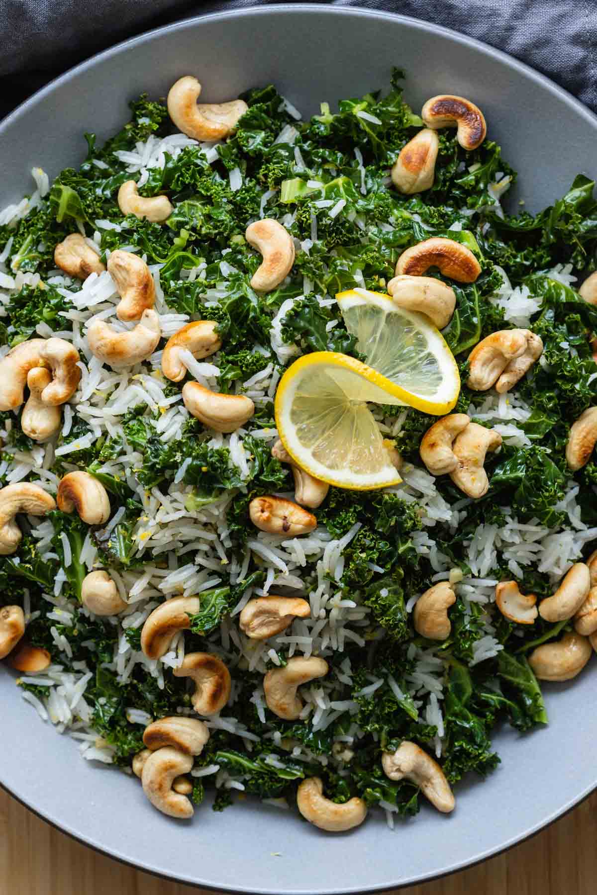 White rice, kale, and cashews in a bowl topped with a slice of lemon.