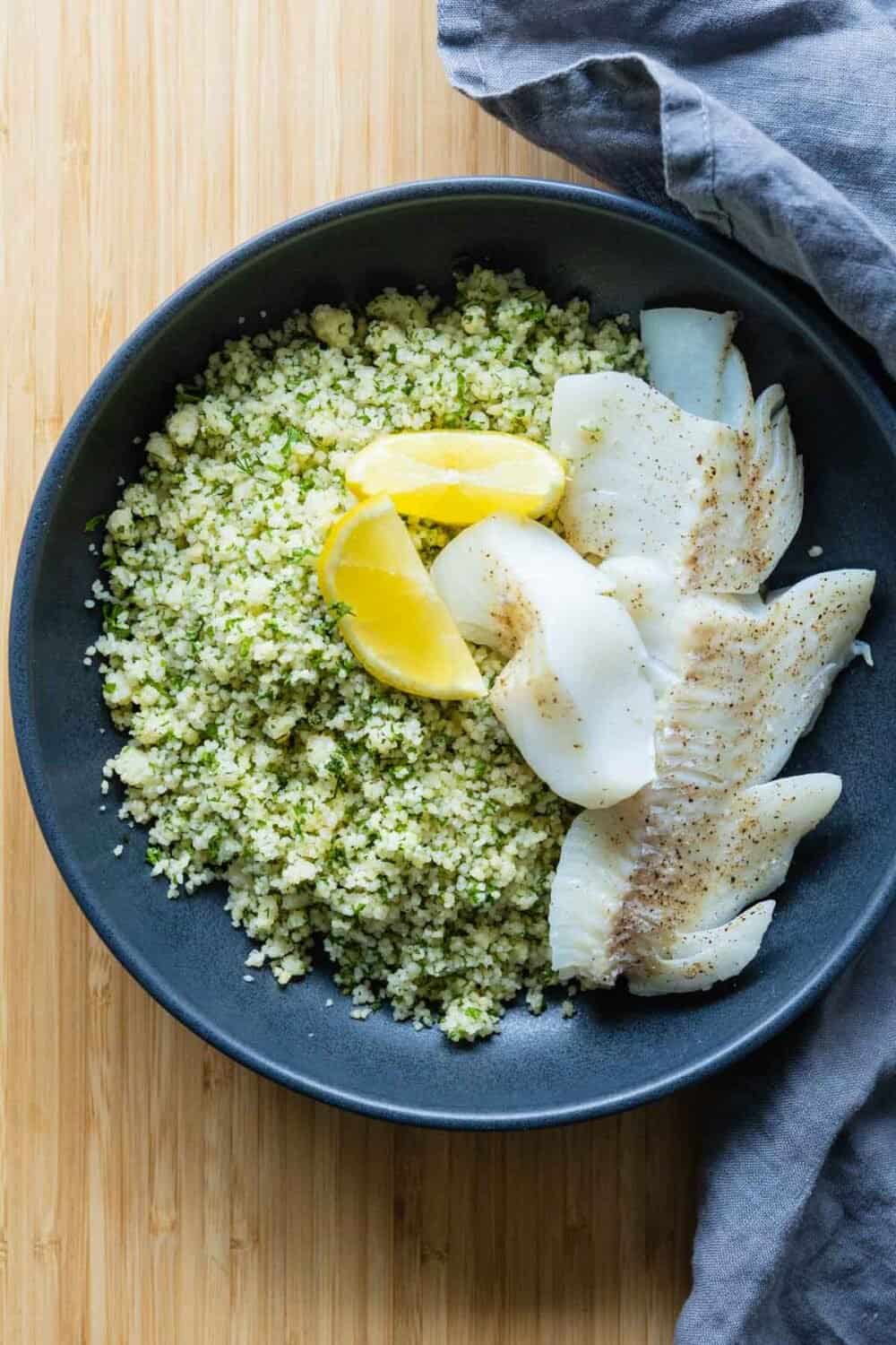 haddock on a bed of couscous with herbs and two lemon sliced on top.