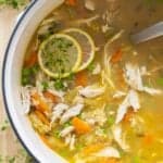 Chicken Soup in a large white pot with two lemon slices placed on top.