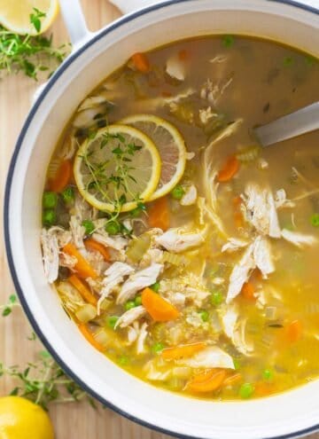 Chicken Soup in a large white pot with two lemon slices placed on top.