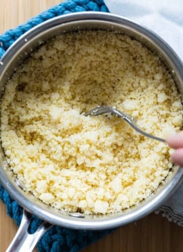 Stainless steel pot with cooked couscous and fork inside fluffing the couscous.