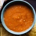 salsa roja in a blue bowl surrounded by tortilla chips.