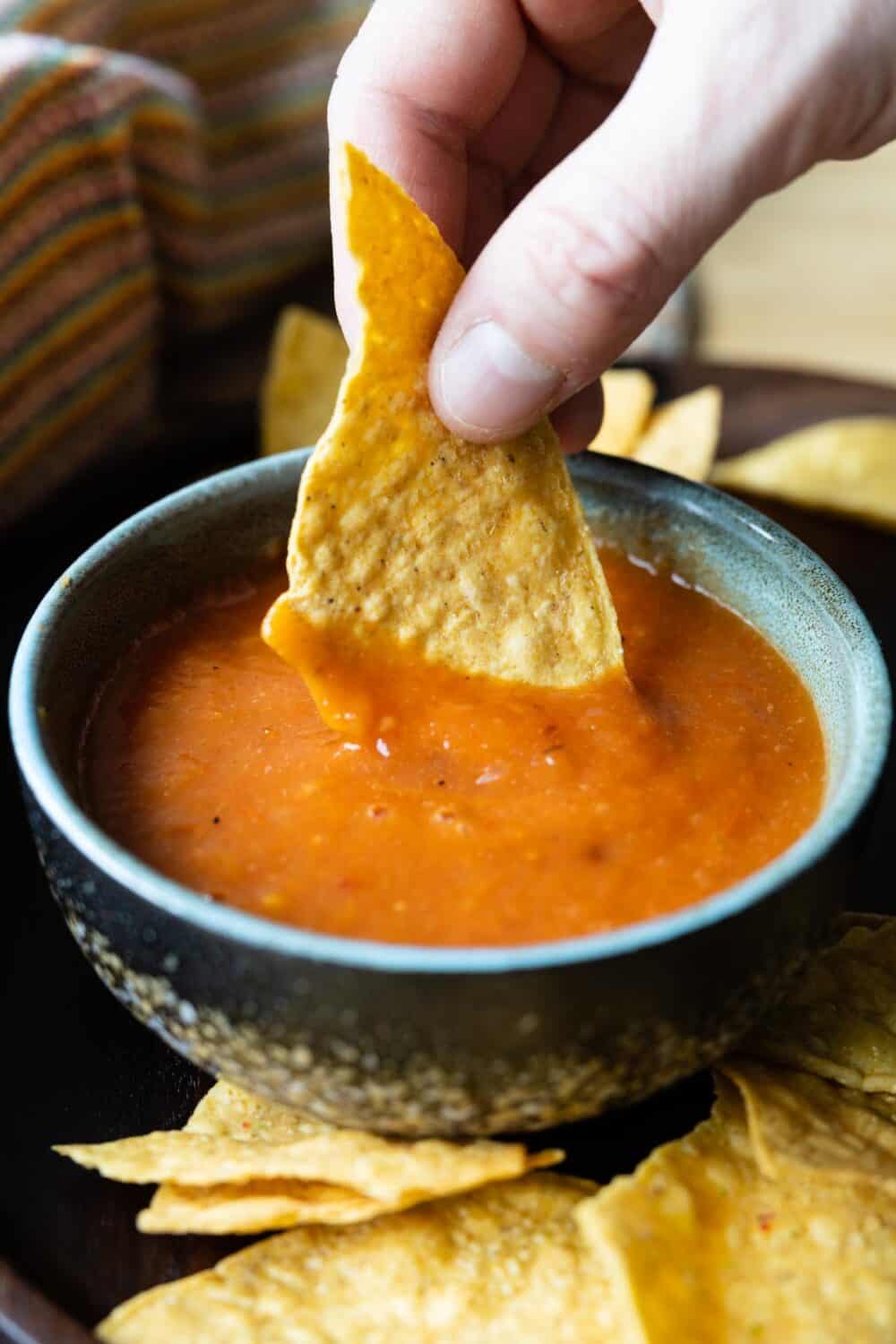 tortilla chip being dipped into salsa roja.