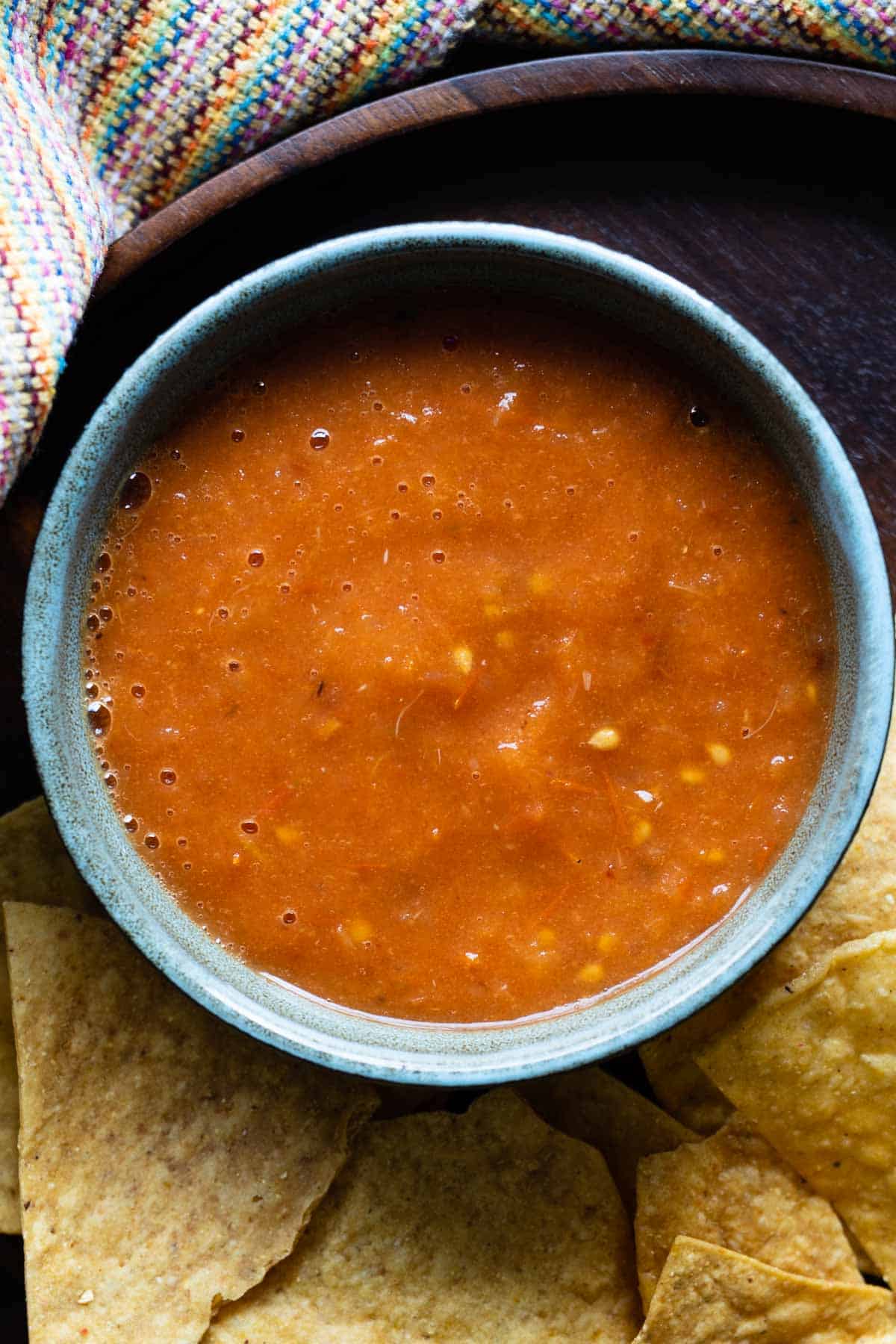 salsa roja in a blue bowl surrounded by tortilla chips.