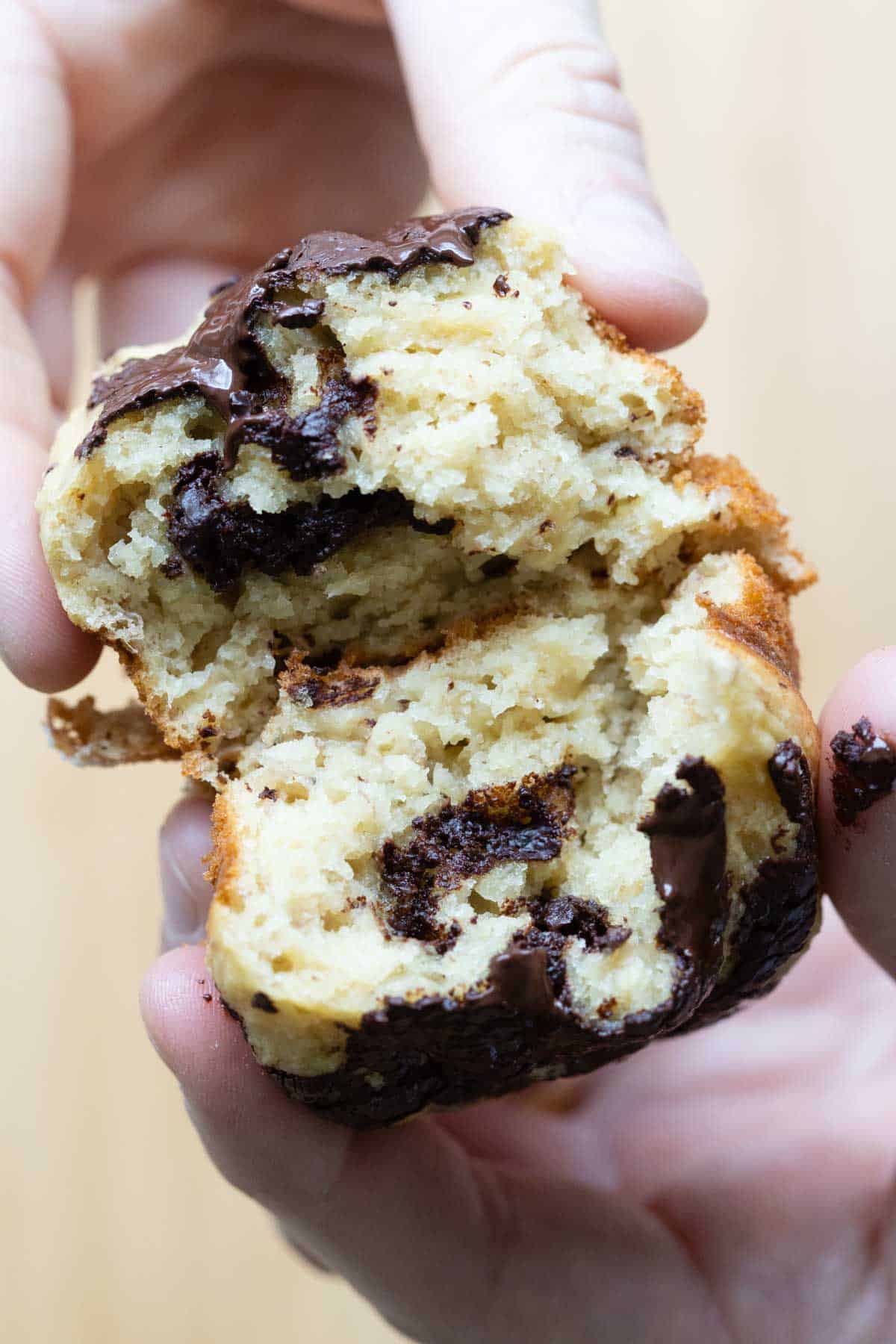 hands pulling apart a healthy banana muffin showing inside texture and dark chocolate bits.