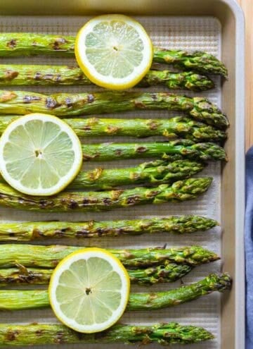 grilled asparagus on a baking sheet with lemon slices on top.