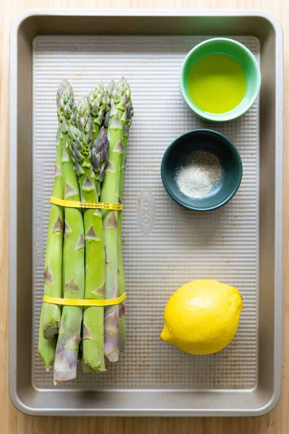Ingredients to make grilled asparagus laid out on a baking sheet.