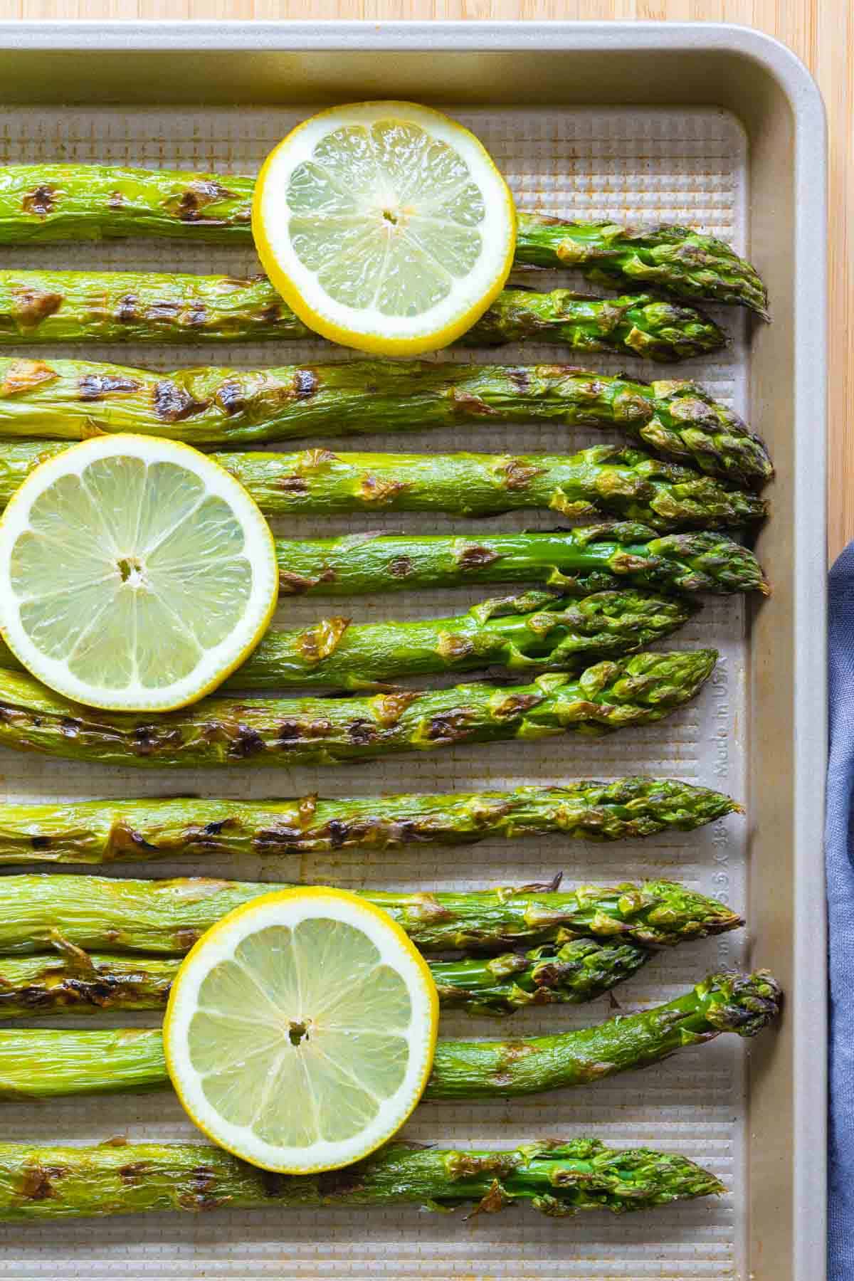 grilled asparagus on a baking sheet with lemon slices on top.