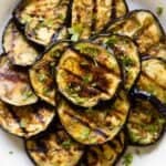 Grilled eggplant rounds stacked on a plate.