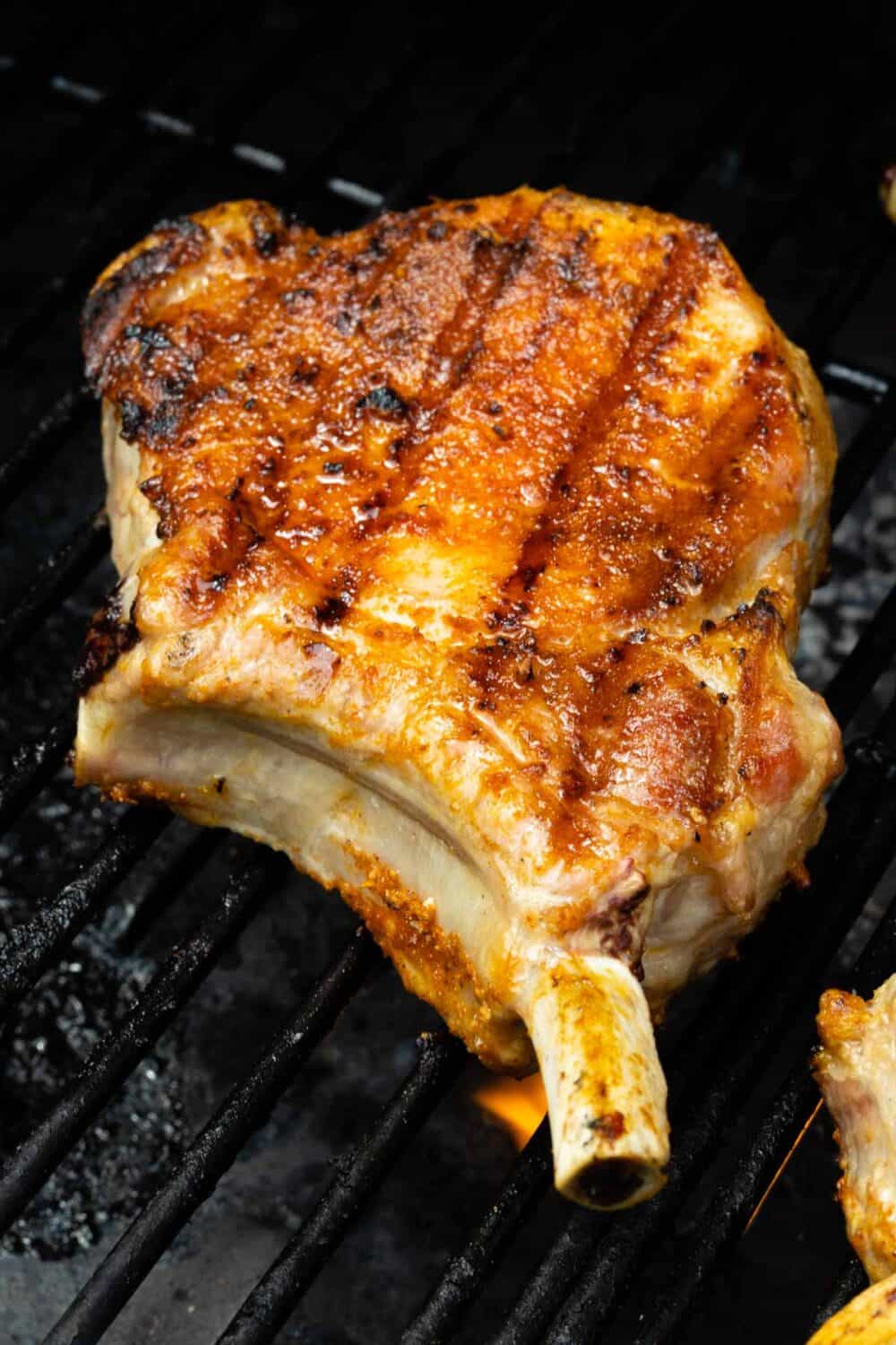 Grilled pork chop on a grill grate and fire underneath.