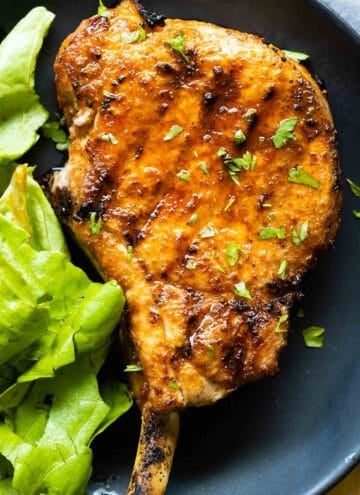 Grilled pork chop on a plate and green lettuce on the side.