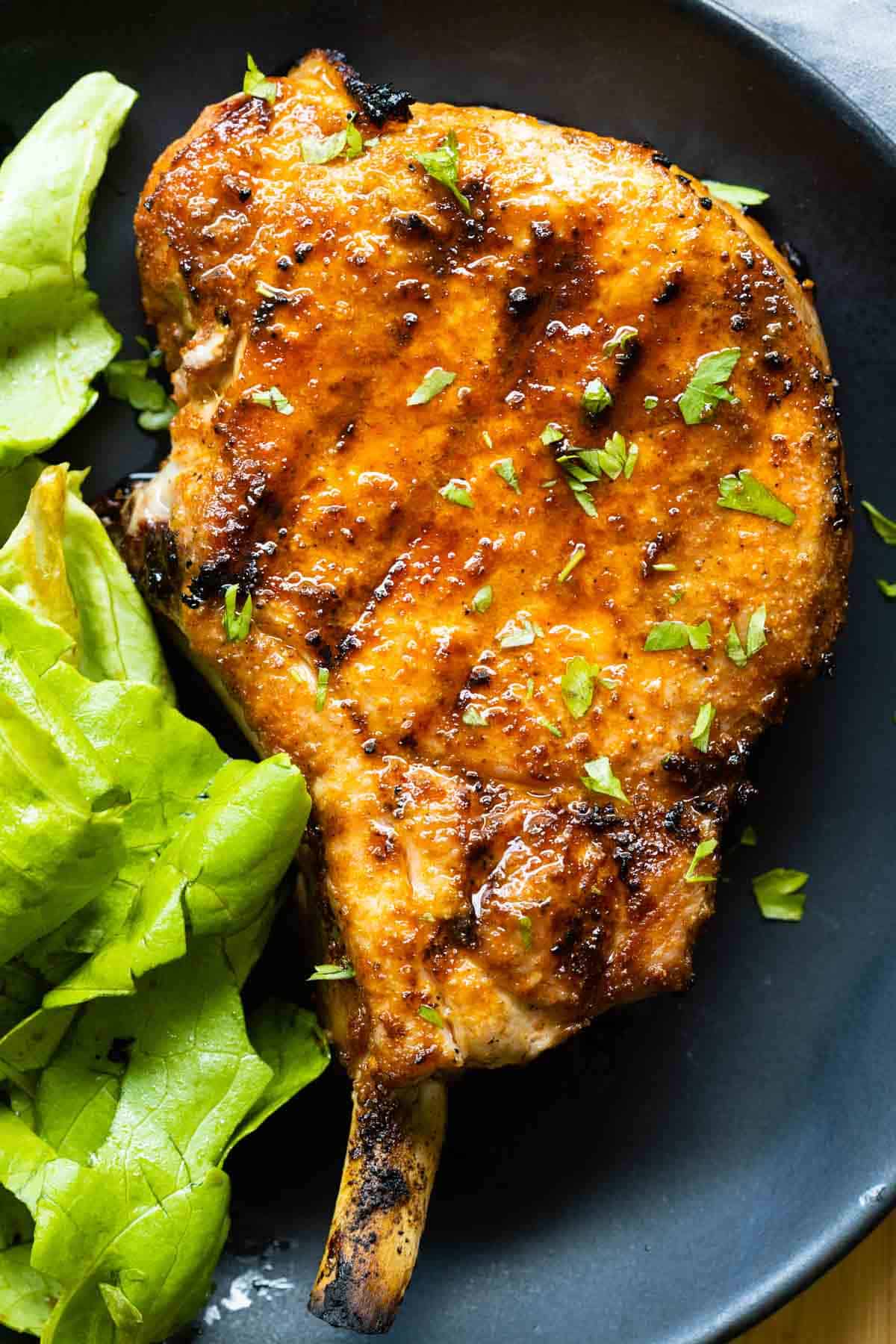 Grilled pork chop on a plate and green lettuce on the side.