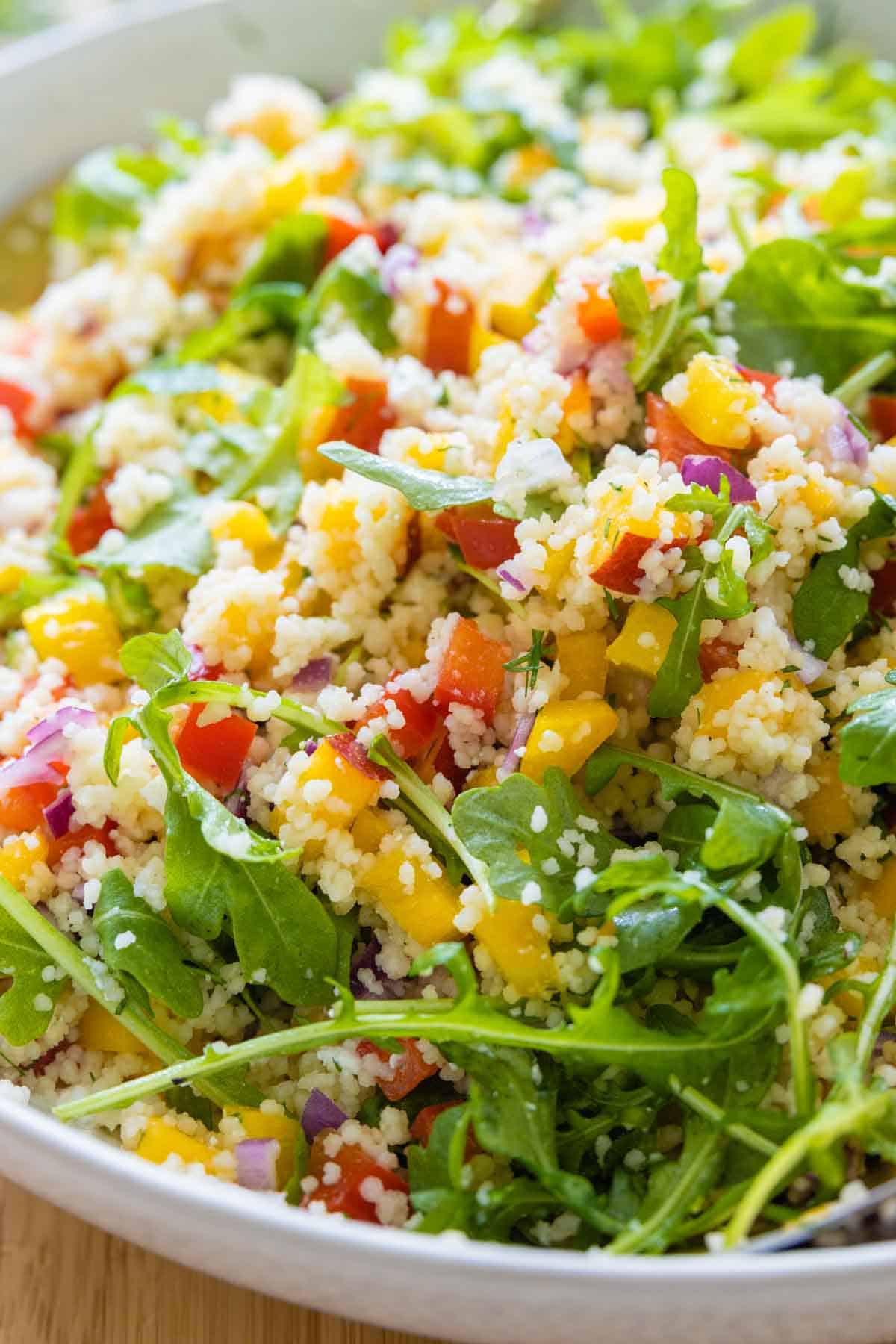 Mixed up couscous salad with arugula in a salad bowl.