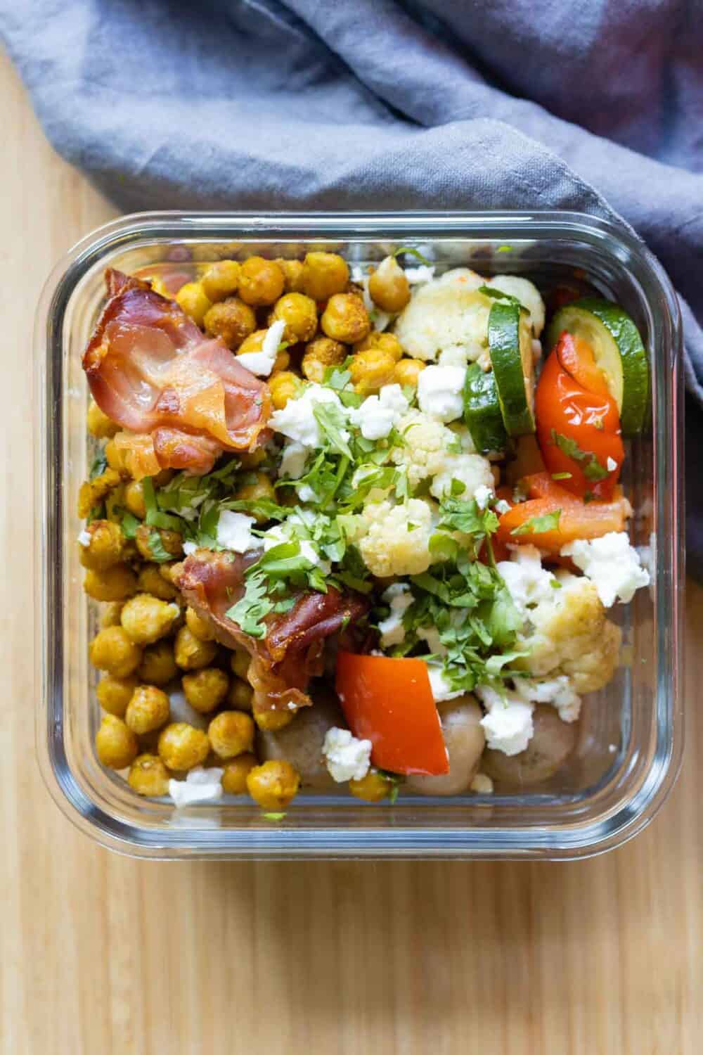 Glass meal prep container filled with chickpeas, vegetables, and prosciutto.