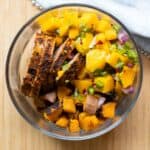 Round glass meal prep bowl filled with pork, mango, and sweet potato.