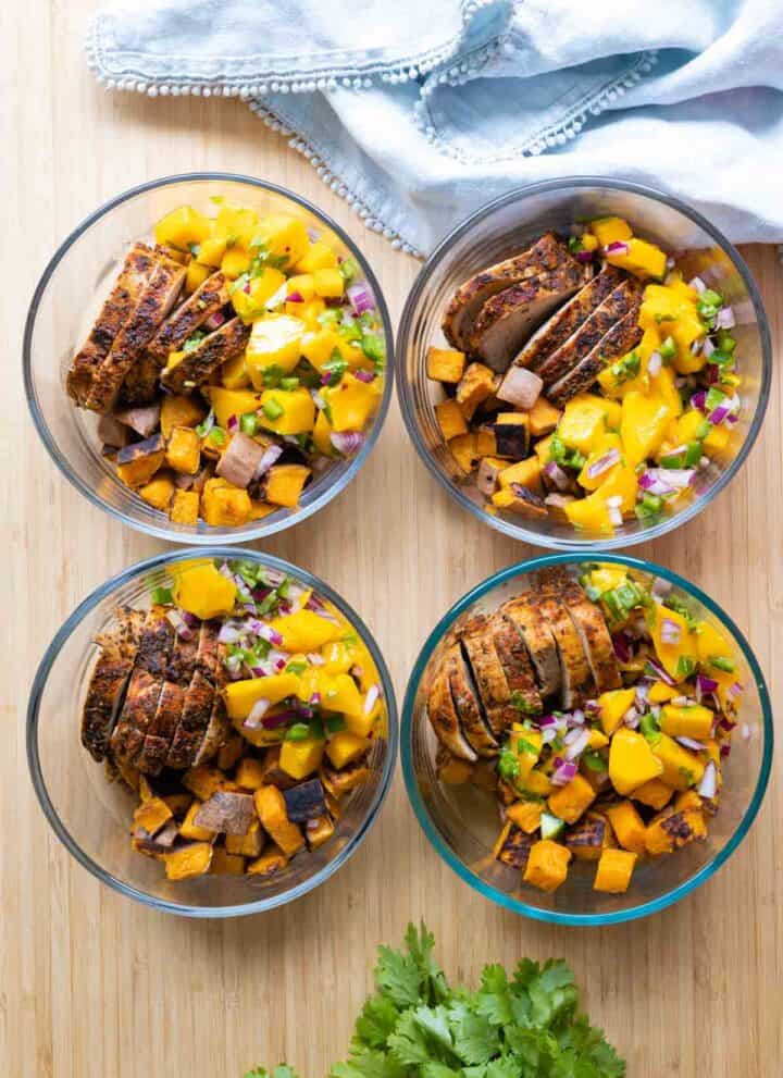 Four meal prep bowls filled with pork, mango, and sweet potatoes.