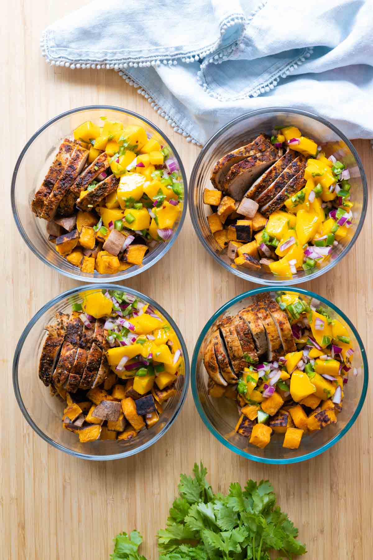 Four meal prep bowls filled with pork, mango, and sweet potatoes.