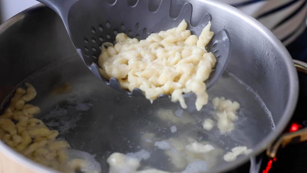 German Spaetzle being lifted out of water with slotted spoon.