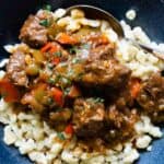 German Goulash on top of Spaetzle in a blue soup bowl.