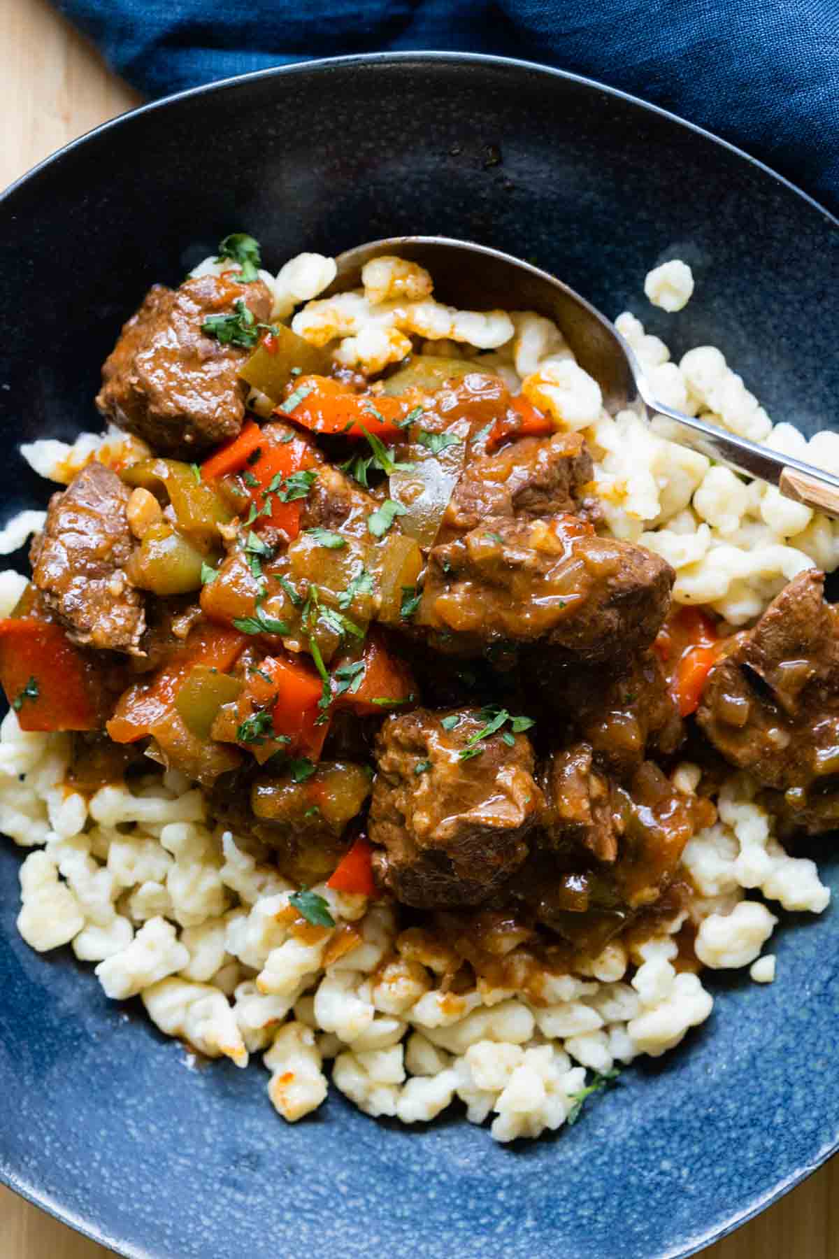 German Goulash on top of Spaetzle in a blue soup bowl.