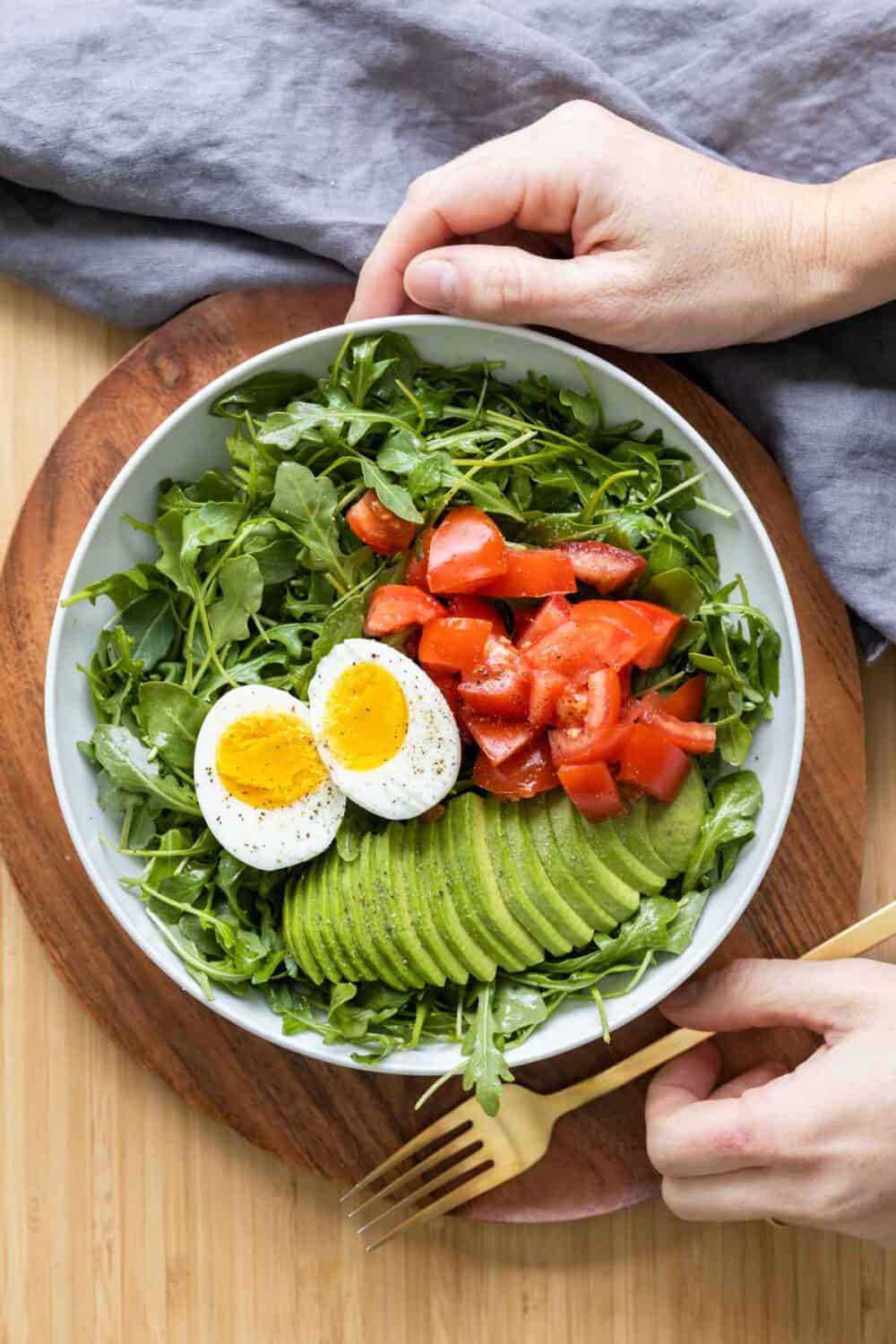 Breakfast salad in a white salad bowl held by hands.