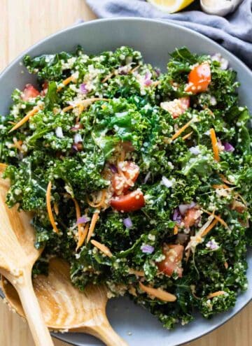 Kale Quinoa Salad in a grey salad bowl with wooden spoons.