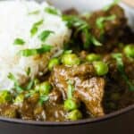 Close-up image of seco de carne in a shallow bowl with white rice in the back.