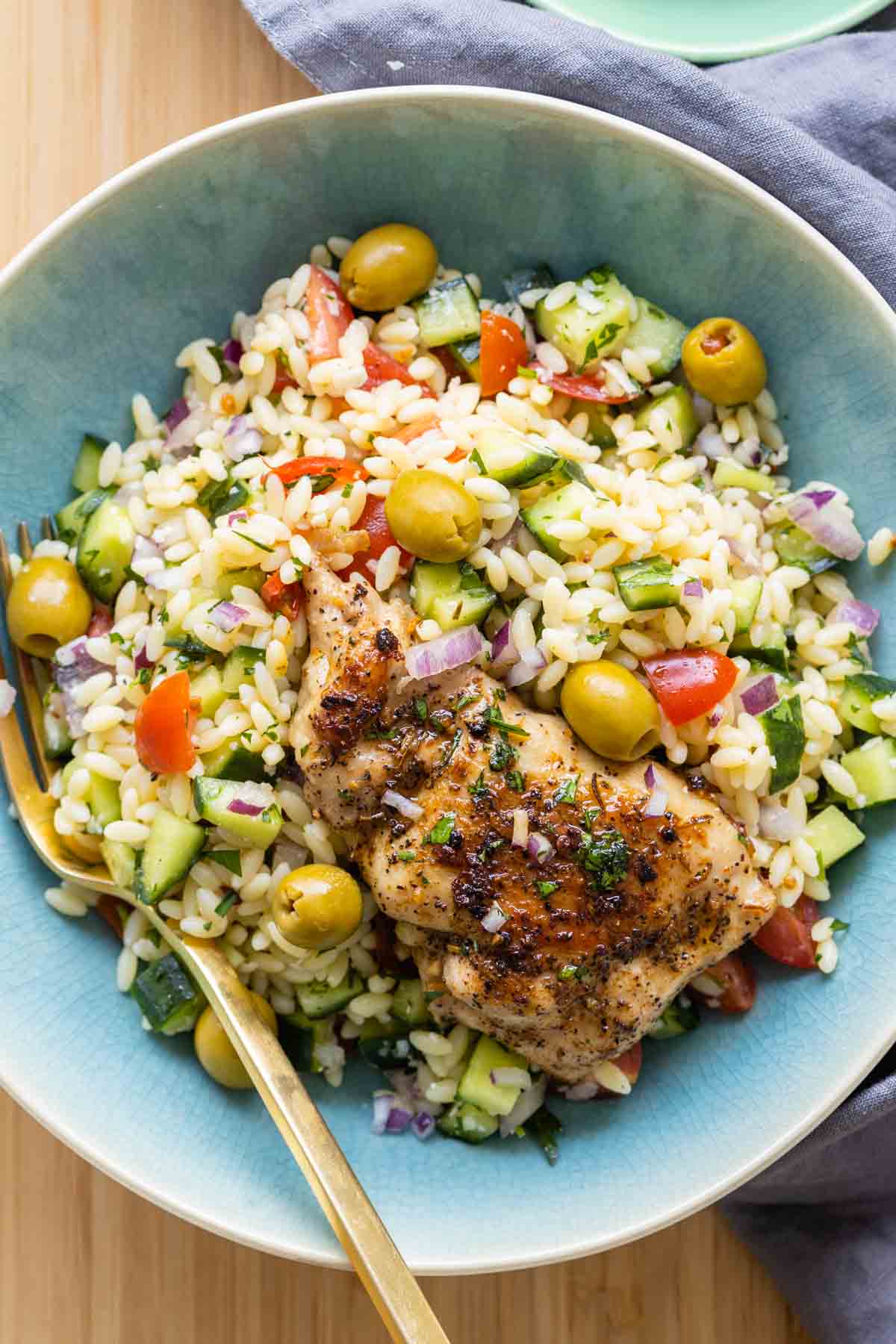 Mediterranean Chicken Orzo in a blue bowl with a golden fork.