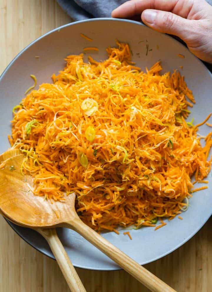 Grated Carrot Salad in a large grey salad bowl with two wooden spoons.