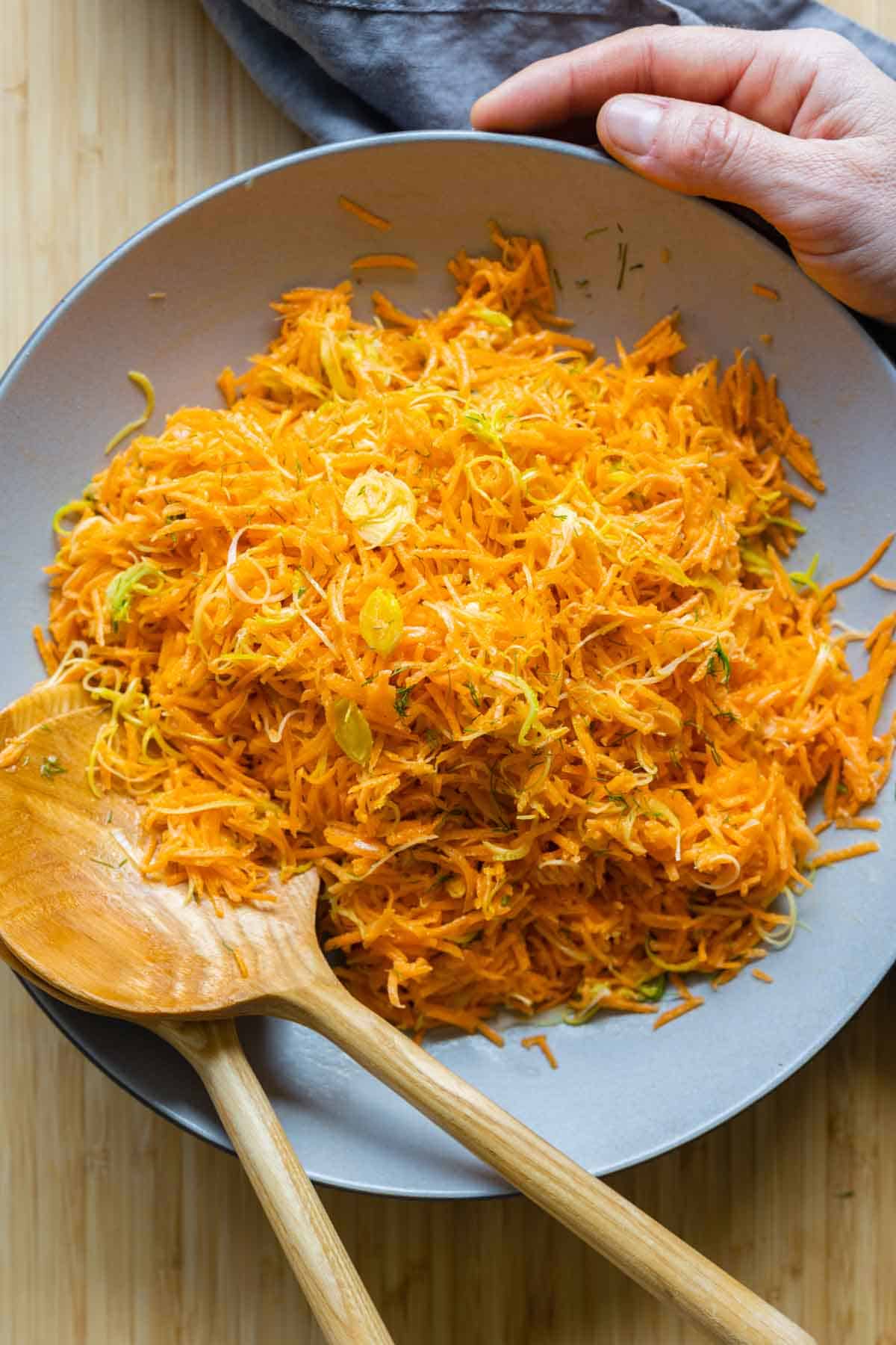 Grated Carrot Salad in a large grey salad bowl with two wooden spoons.