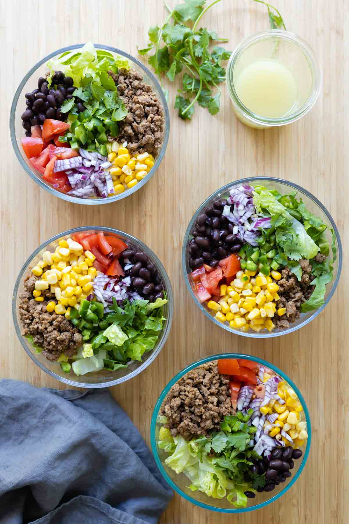 Four Meal Prep Burrito Bowls and a jar with dressing on a kitchen counter.