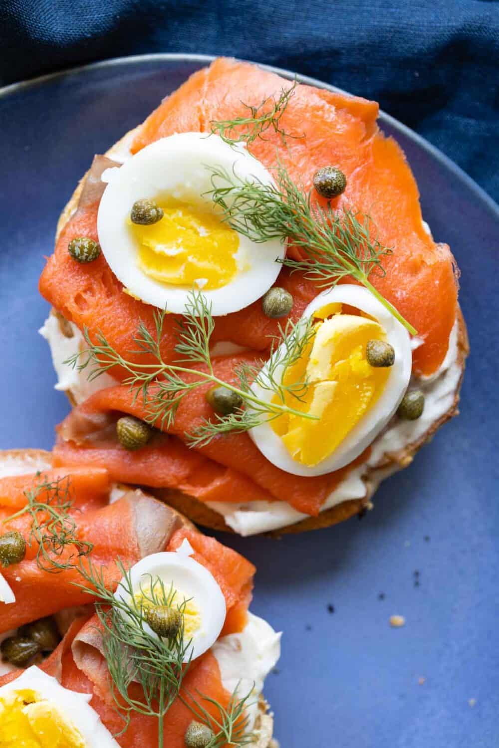 Salmon Bagel with hard-boiled egg, dill, and capers on top.