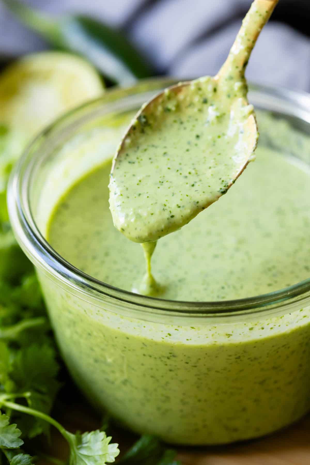 Aji Verde Sauce in a glass bowl with a golden spoon being dipped into it.