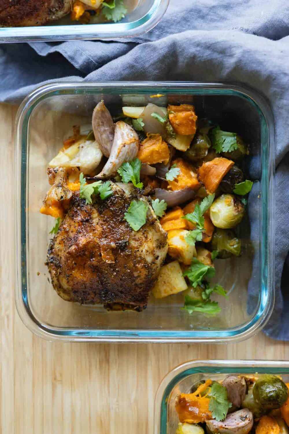 Chicken Thigh on top of root vegetables in a square glass container.