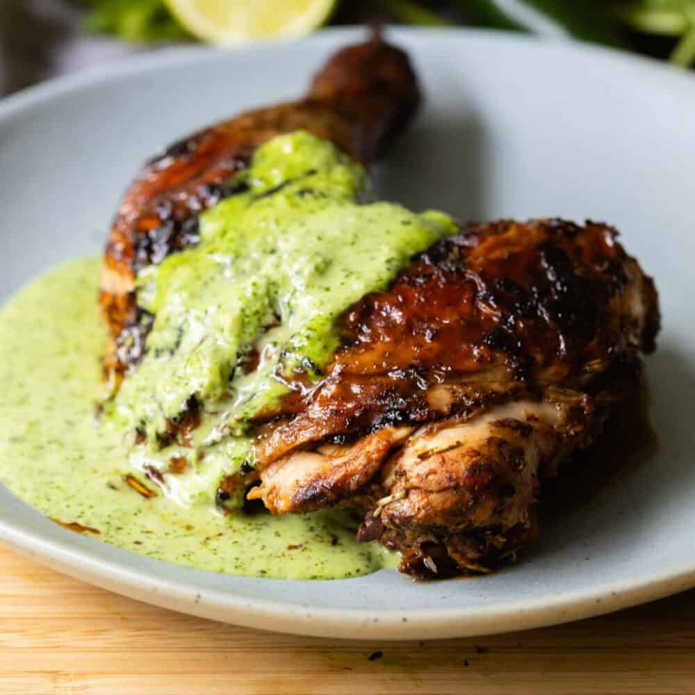 Grilled Chicken Leg with ají verde sauce on top on a light blue plate.