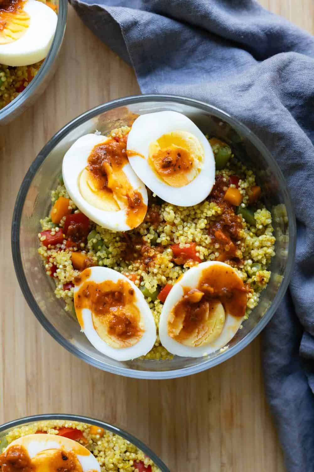 Veggie Quinoa with hard-boiled eggs in a round glass container.