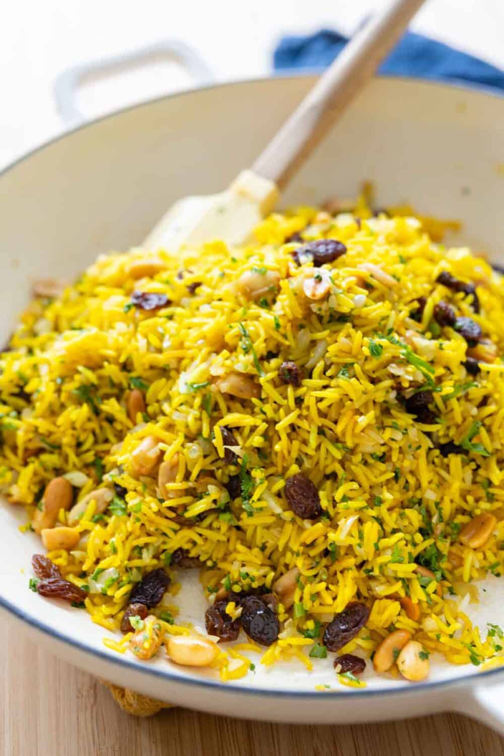 Yellow rice with onions, raisins, peanuts, and parsley in a large white pan.