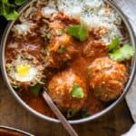 Albondigas in tomato sauce served over white rice and sprinkled with cilantro in a bowl. One meatball cut open to show the egg inside.