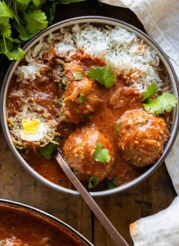 Albondigas in tomato sauce served over white rice and sprinkled with cilantro in a bowl. One meatball cut open to show the egg inside.