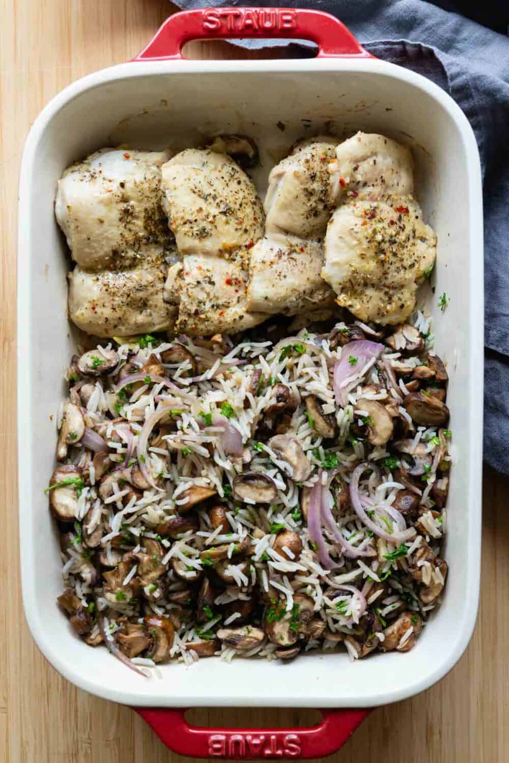 Mushroom rice and baked chicken breasts in a red and white baking dish.